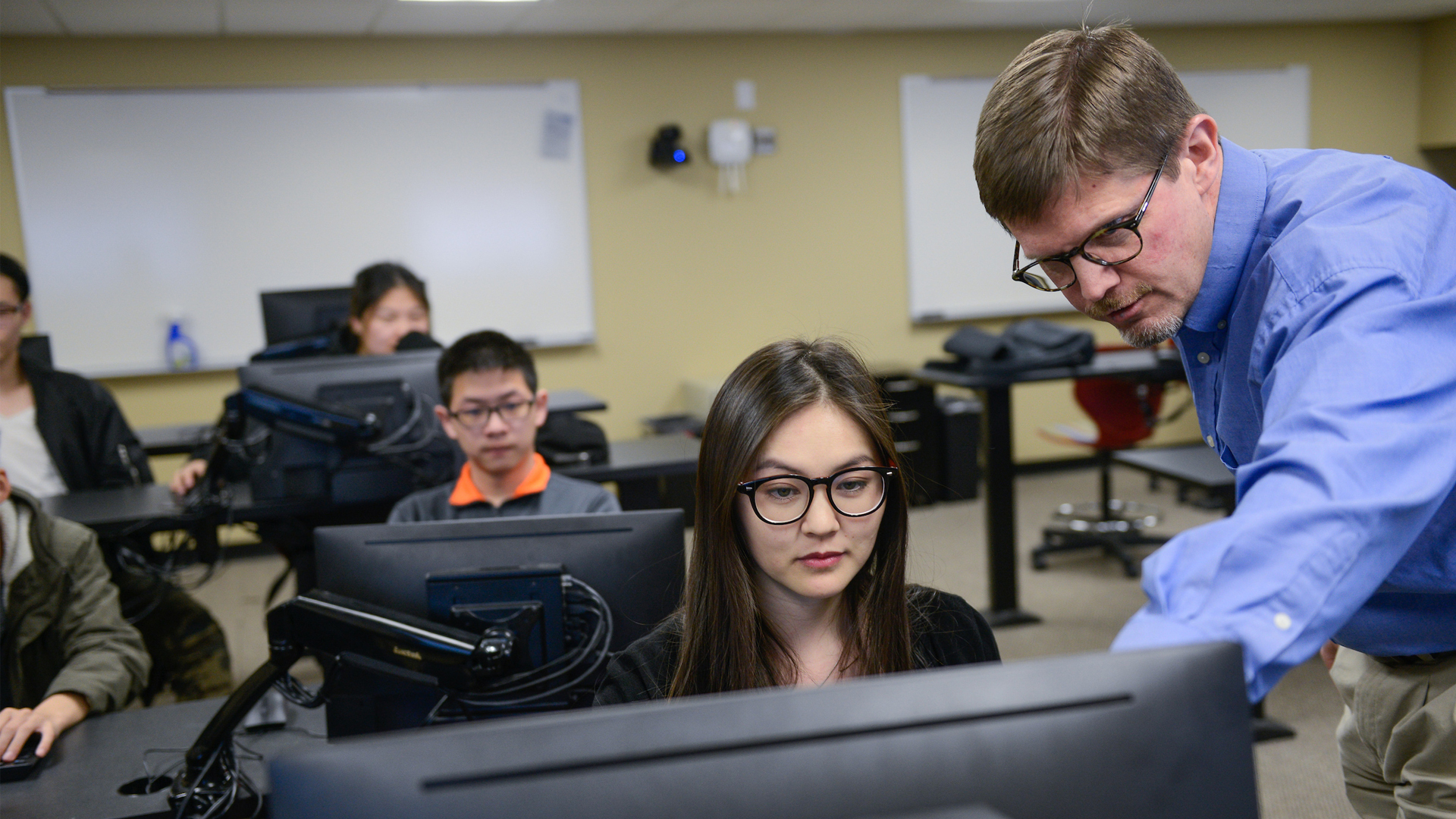An instructor walks a young professional through a computer program in a classroom setting.