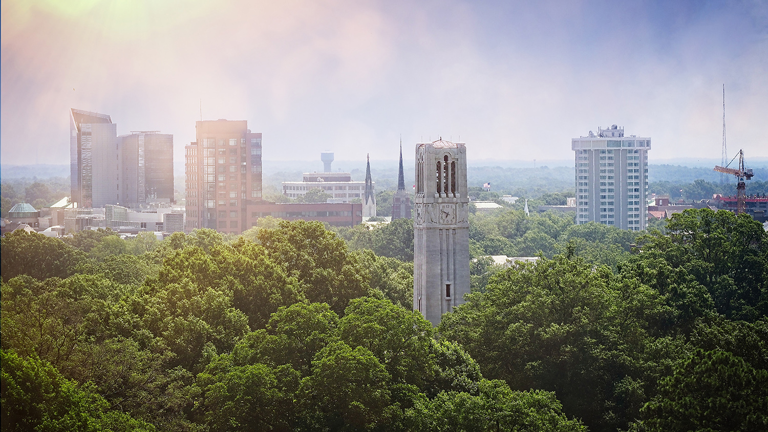 The NC State belltower sits in front of the city of Raleigh skyline as seen from a DH Hill library window.